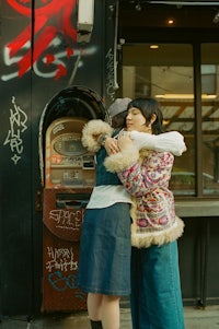 two women hugging in front of a building