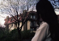 a woman with long hair standing in front of a house