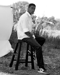 a black and white photo of a man sitting on a stool